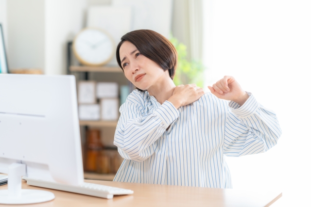 自宅パソコンの前で肩を回す女性