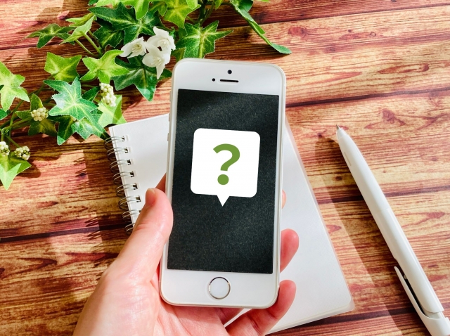 クエスチョンマークが表示されたスマホと、それを持つ手