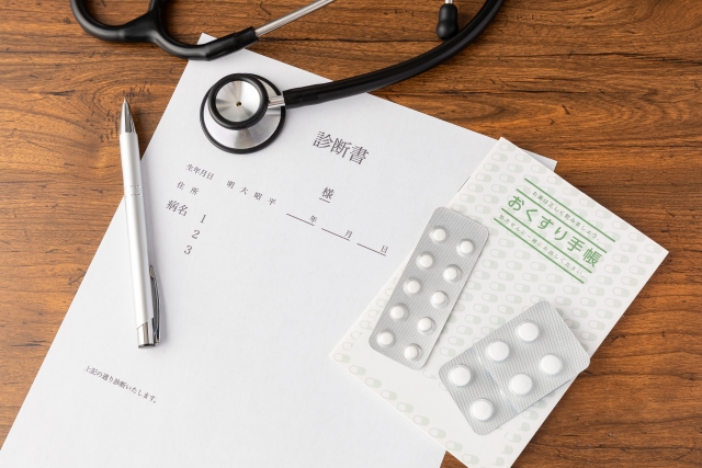 デスクに並ぶ聴診器と診断書、薬、おくすり手帳